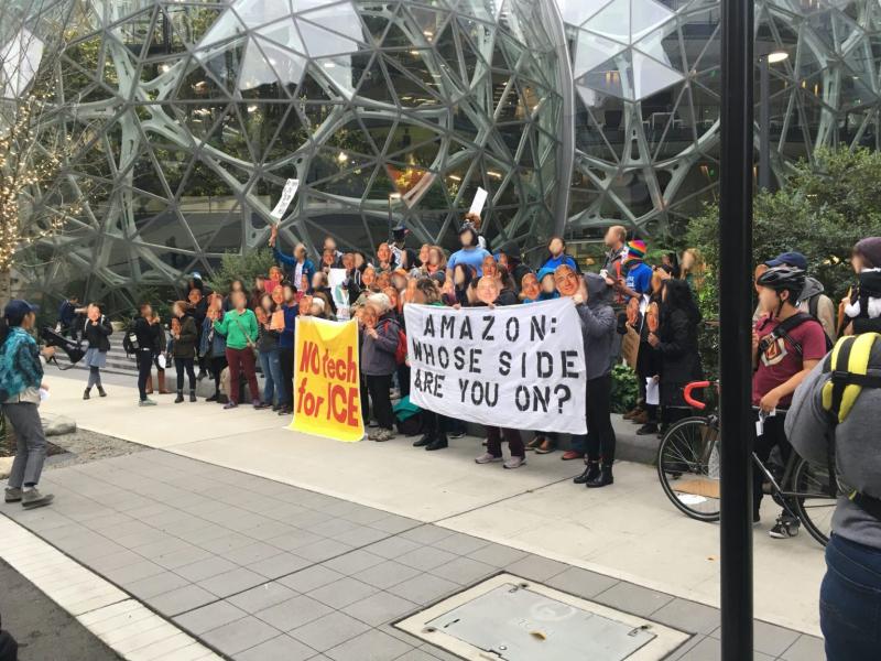 Image of people demonstrating in front of Amazon with signs that say No Tech for Ice and Amazon: Whose Side Are You On?
